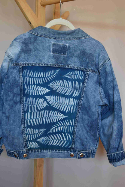 a blue jean jacket hanging on a wooden hanger.