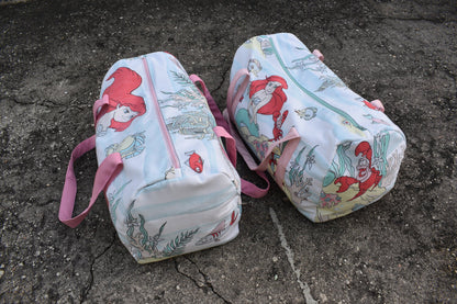 Two duffel bags with mermaids on them.