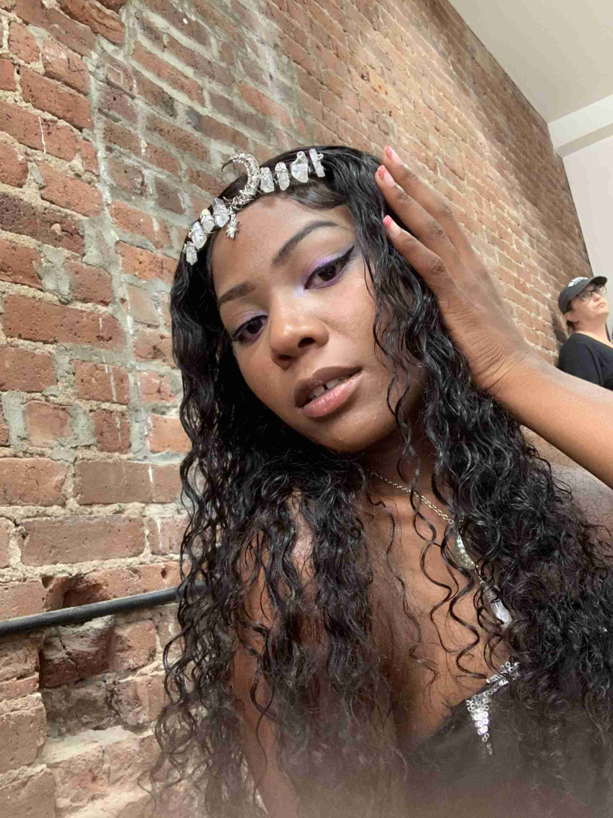 a woman wearing a tiara standing next to a brick wall.