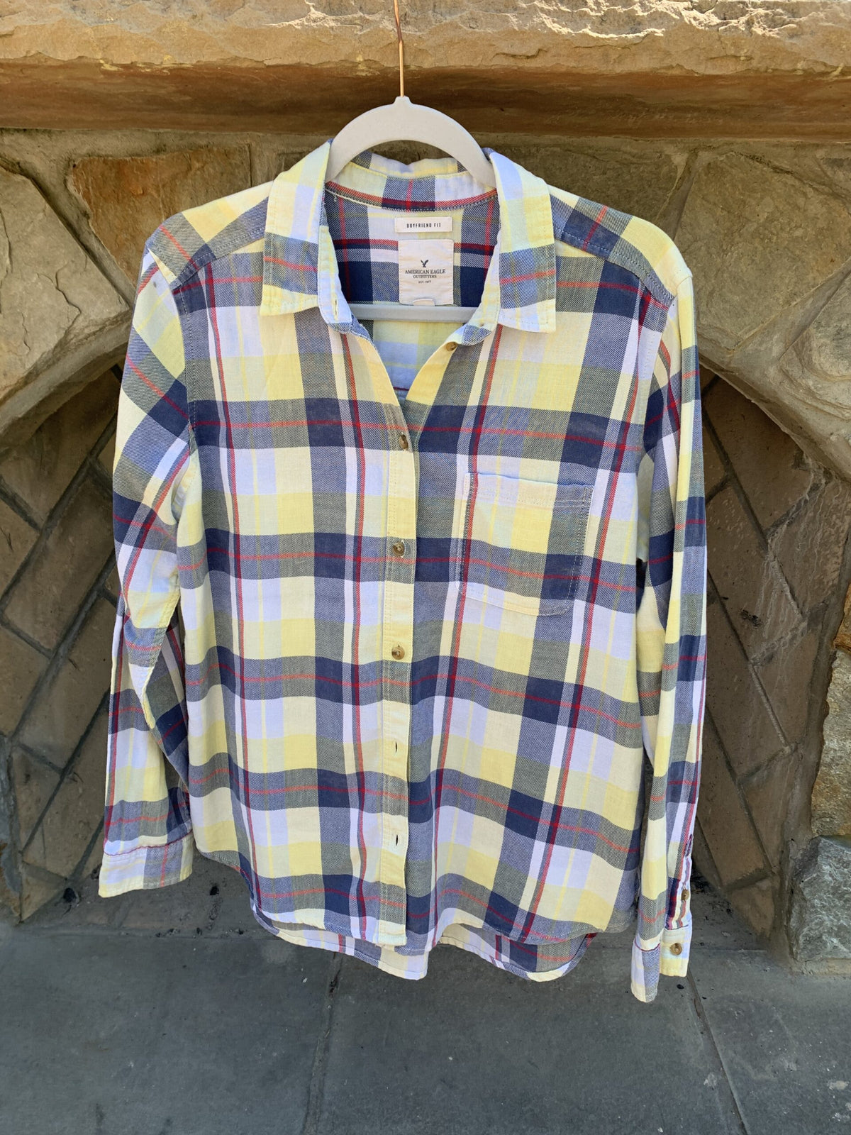 a yellow and blue plaid shirt hanging on a stone wall.