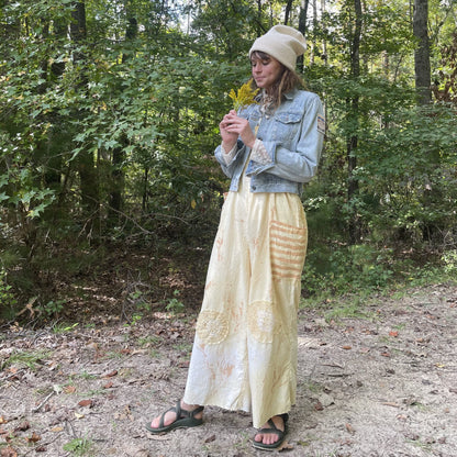 A woman in a yellow skirt standing in the woods.