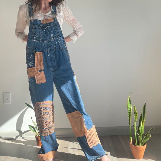 A woman is standing in a room wearing denim overalls.