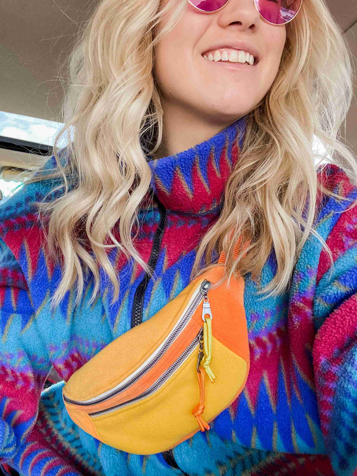a woman wearing a colorful sweater and pink sunglasses.