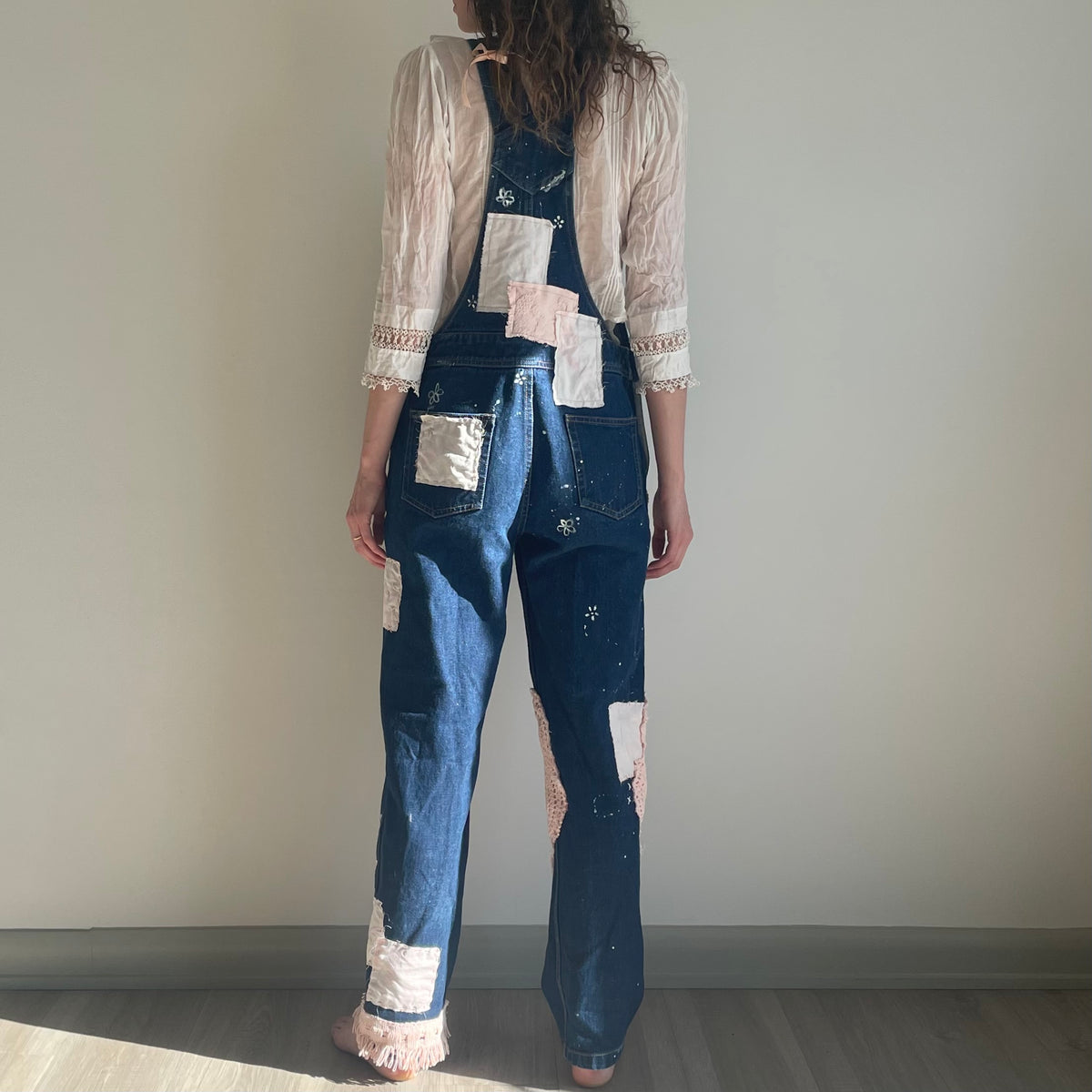 A woman is standing in front of a wall wearing denim overalls.