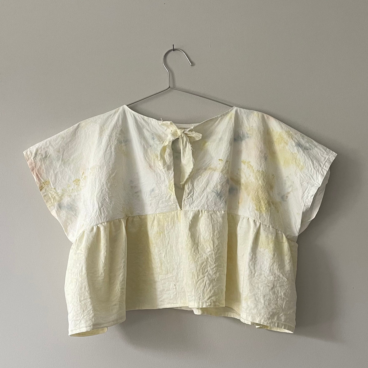 A Yellow Tie-dyed Babydoll Crop Top hanging on a hanger on a wall.