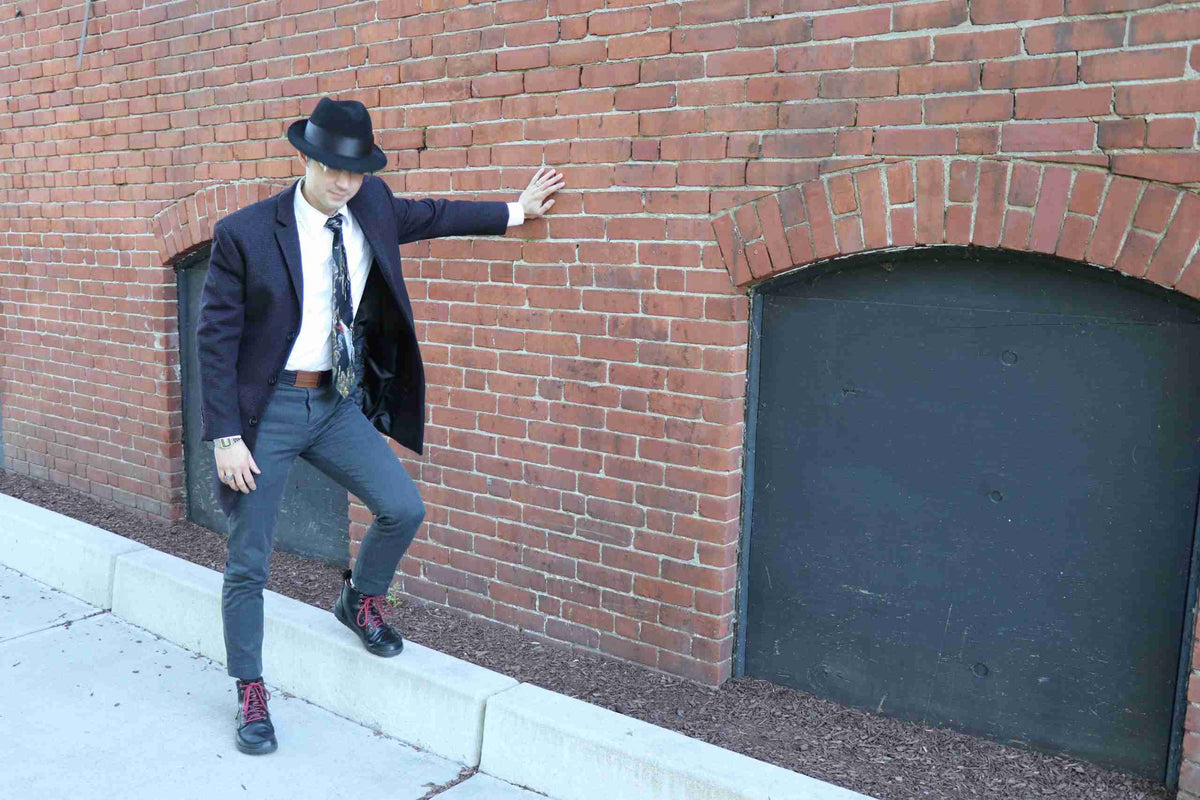 a man in a suit and hat leaning against a brick wall.