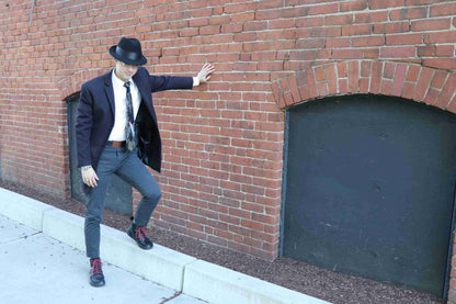 a man in a suit and hat leaning against a brick wall.