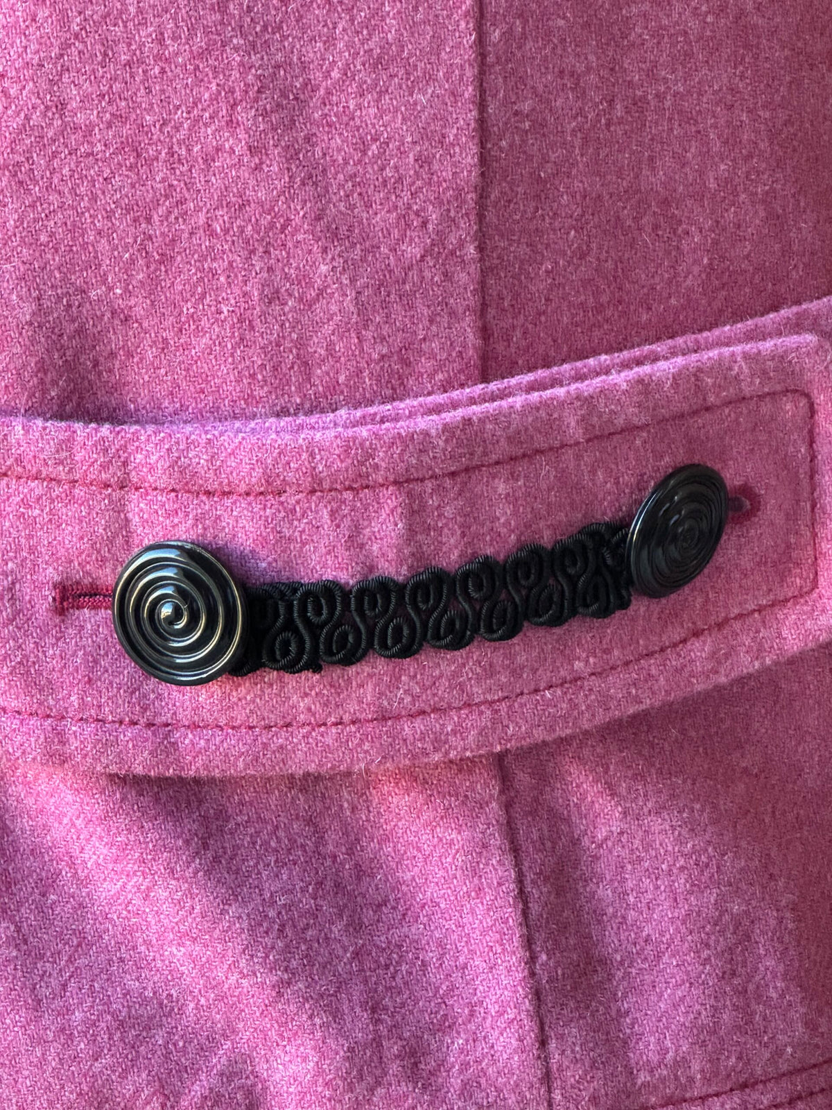 A close up of a pink jacket with black buttons.