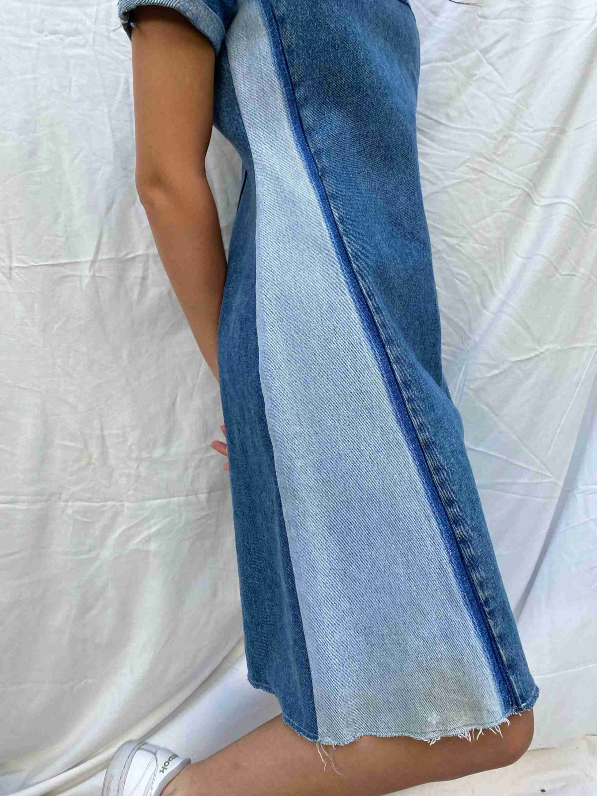 a woman wearing a jean dress and slip on shoes.