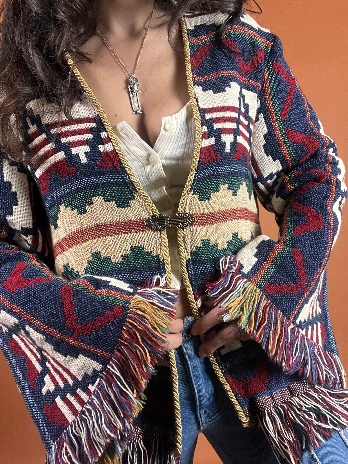 A woman is posing in a colorful sweater with fringes.