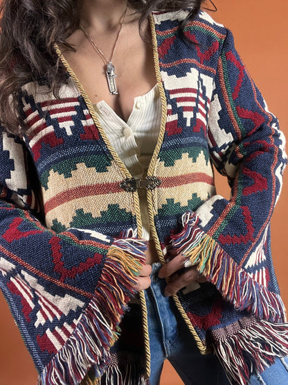A woman is posing in a colorful sweater with fringes.