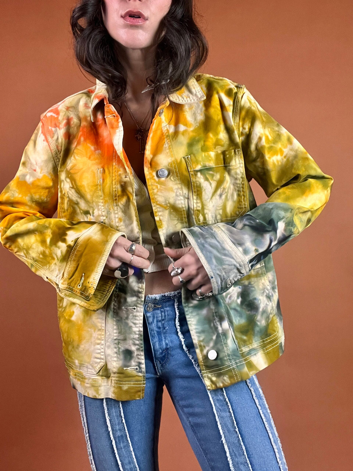 A woman wearing a tie dye jacket and jeans.
