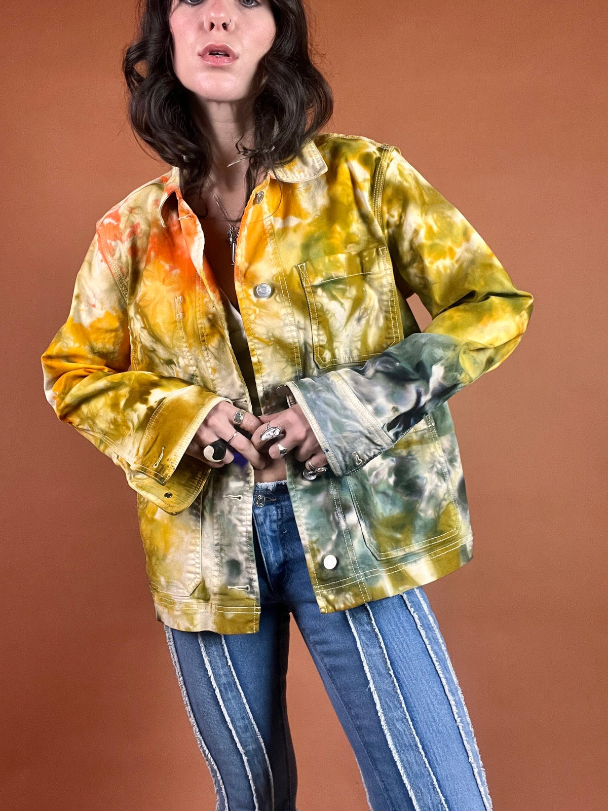 A woman wearing a tie dye jacket and jeans.