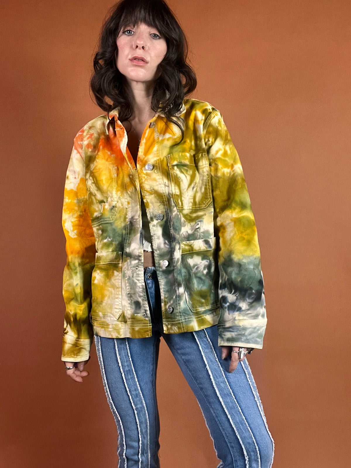 A woman wearing a tie dye jacket and jeans.