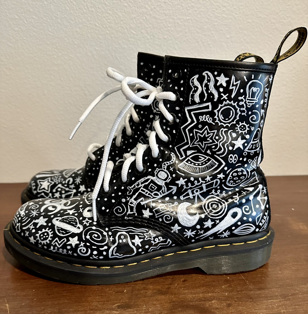 A pair of black and white dr martens boots with doodles on them.