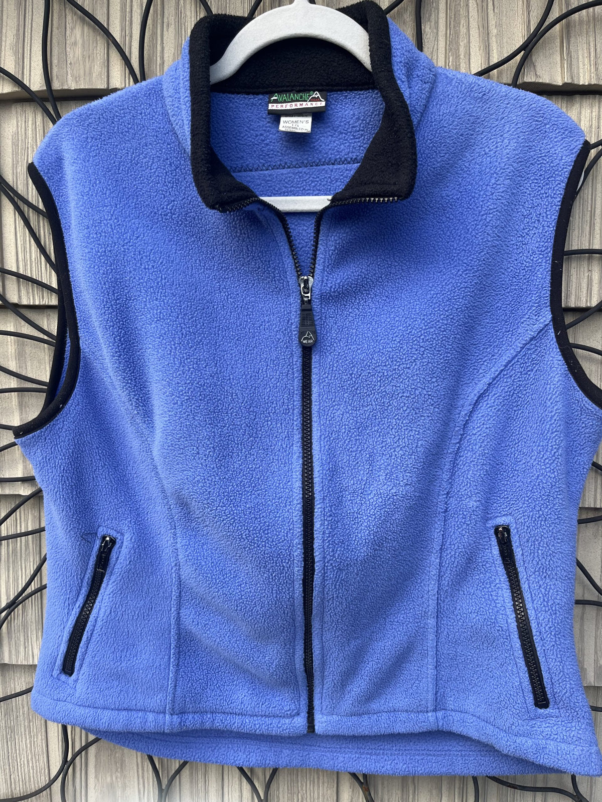 A women's blue flee vest hanging on a wall.