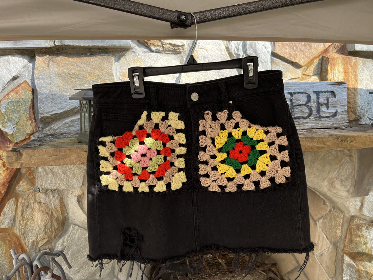 A black denim skirt with crocheted flowers on it.