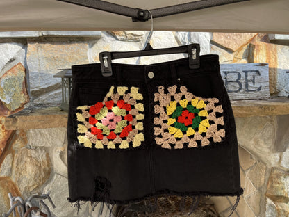 A black denim skirt with crocheted flowers on it.