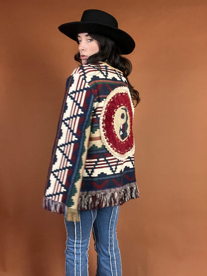 A woman in a cowboy hat and cowboy boots is wearing a colorful sweater.