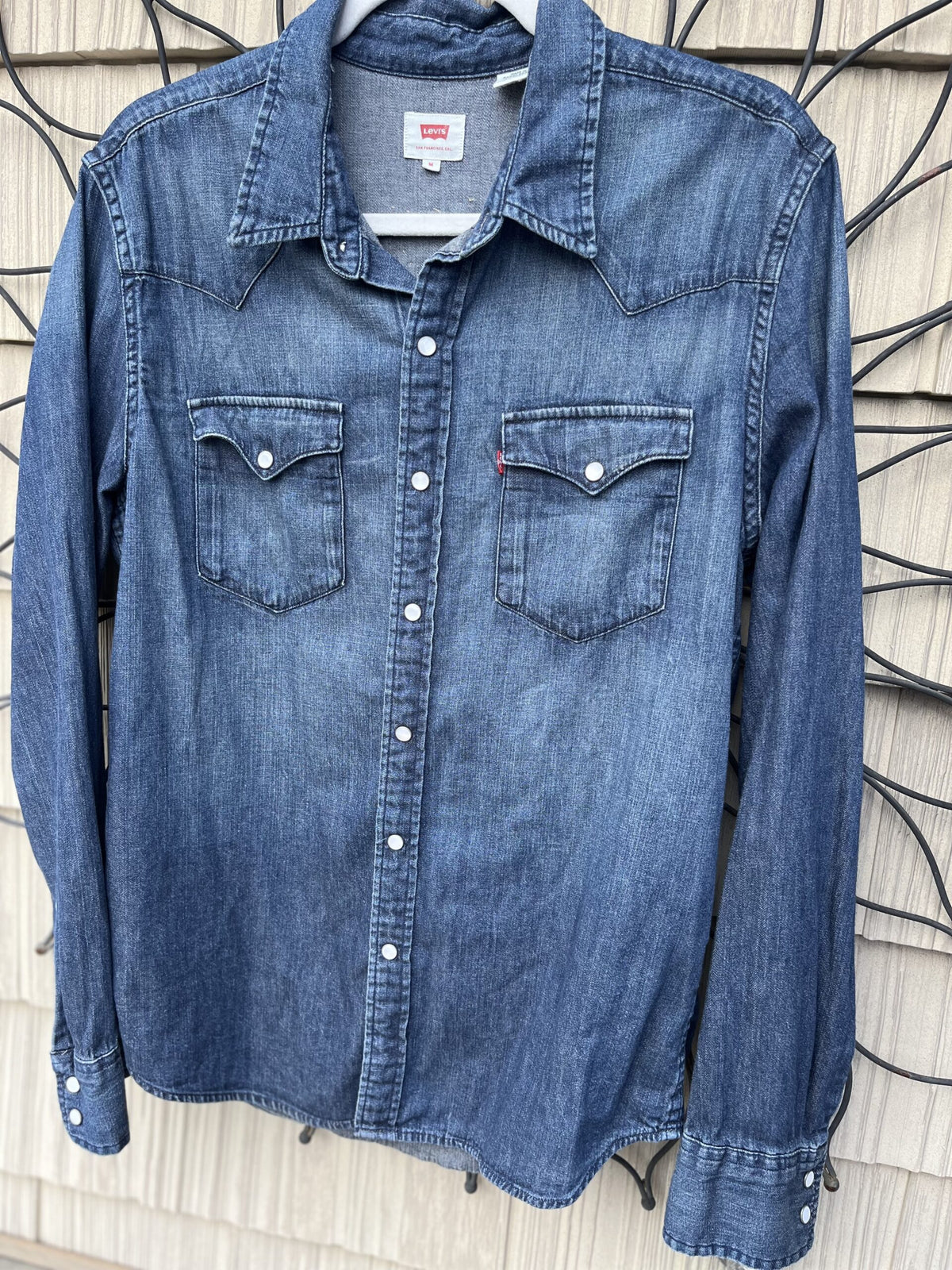A blue denim shirt hanging on a wall.
