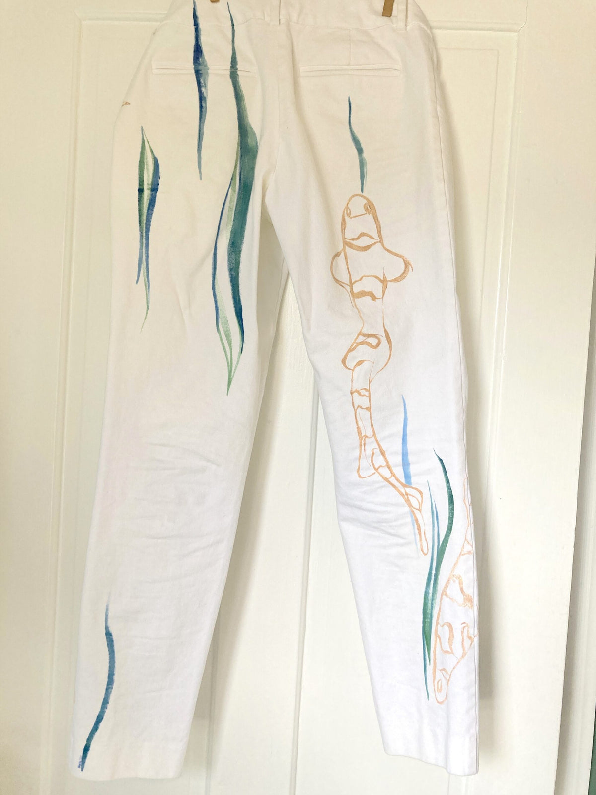 a pair of white pants hanging on a door.