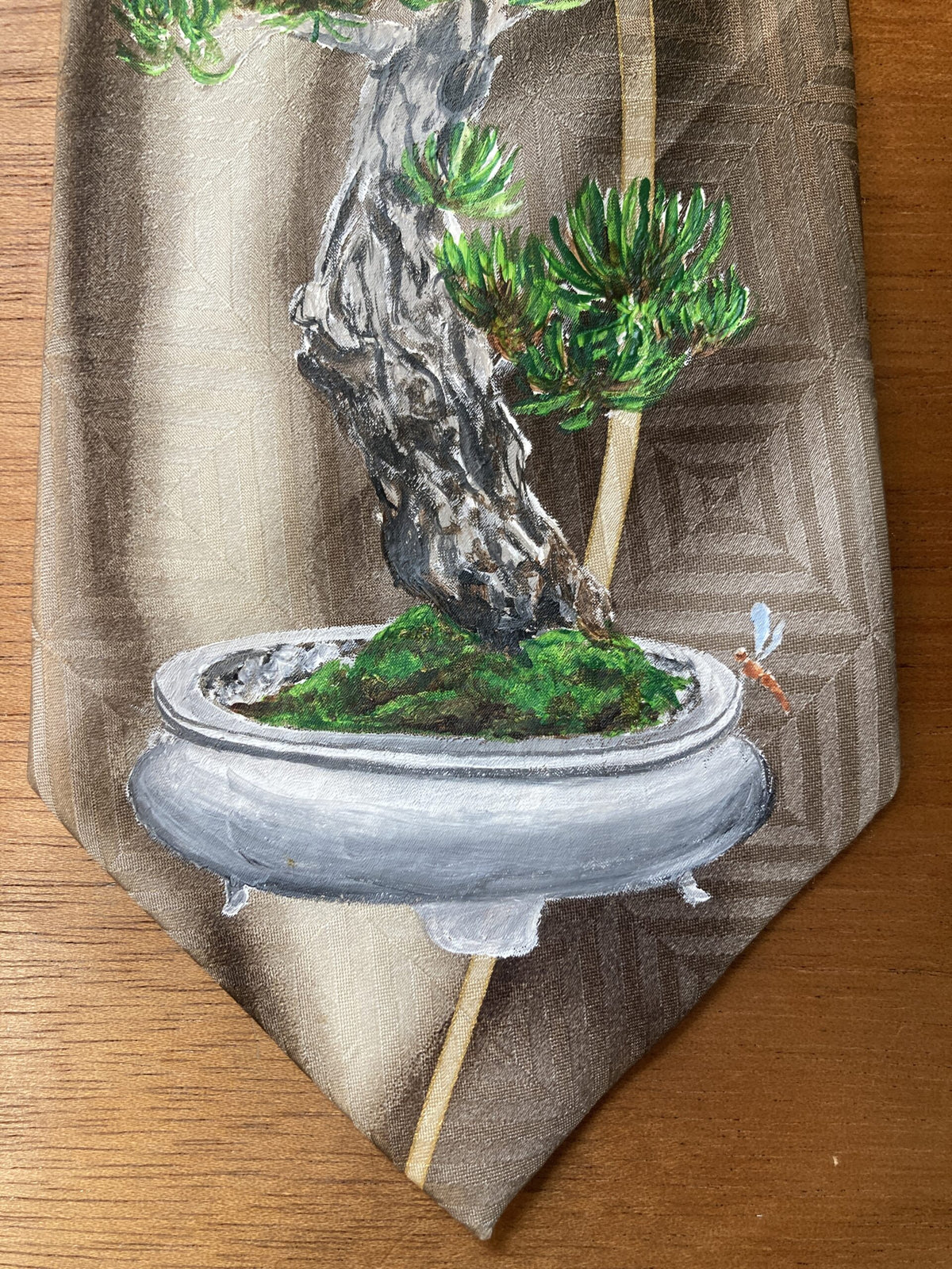 A hand-painted bonsai tree and dragonflies silk tie on a table.