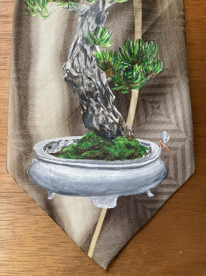 A hand-painted bonsai tree and dragonflies silk tie on a table.