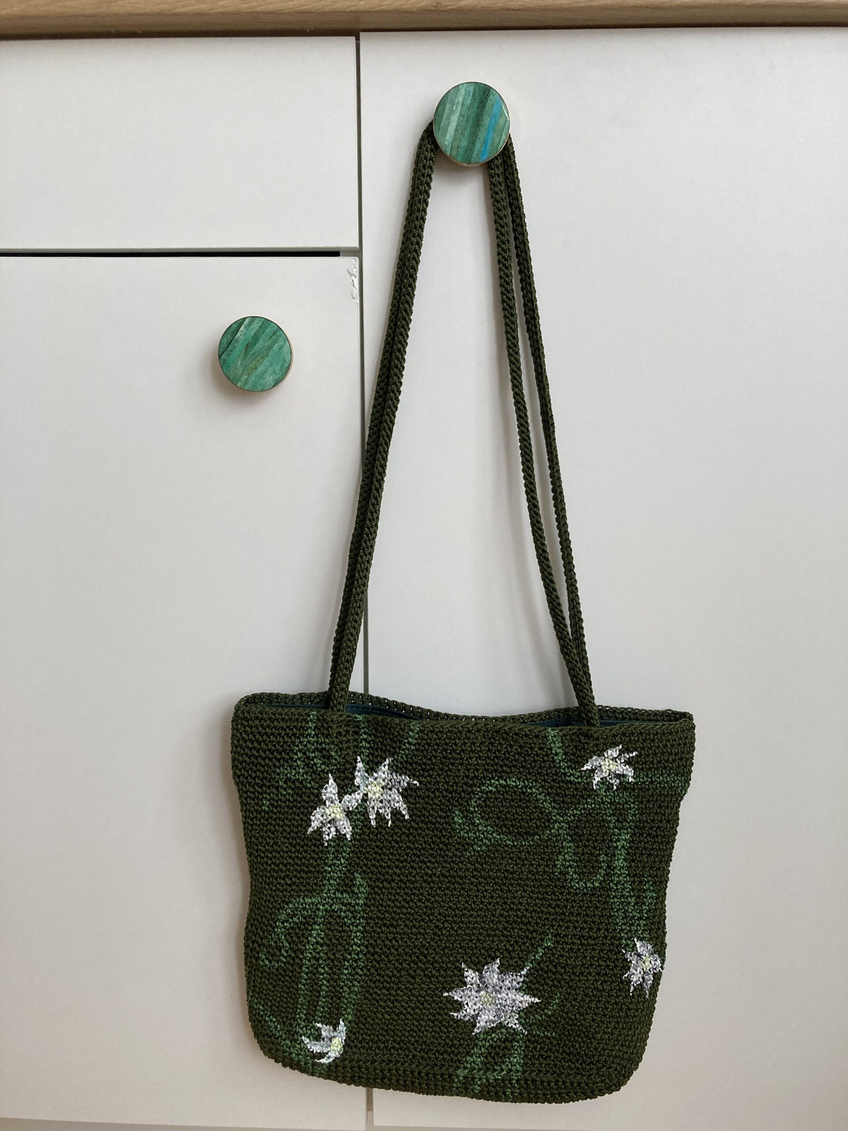 A hand-painted green vines purse hanging on a white cabinet.
