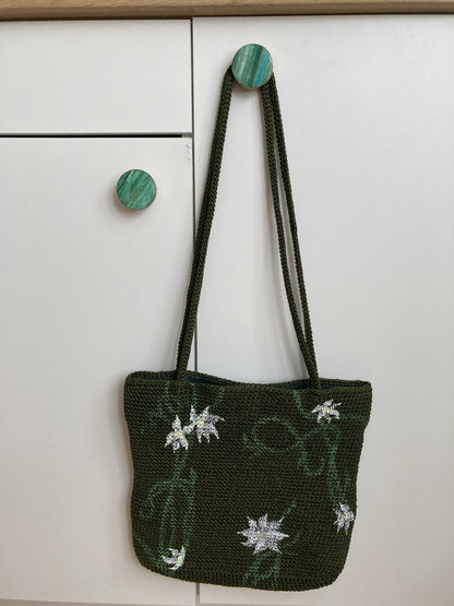 A hand-painted green vines purse hanging on a white cabinet.