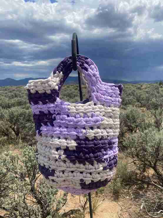 a purple and white crocheted bag hanging from a tree.