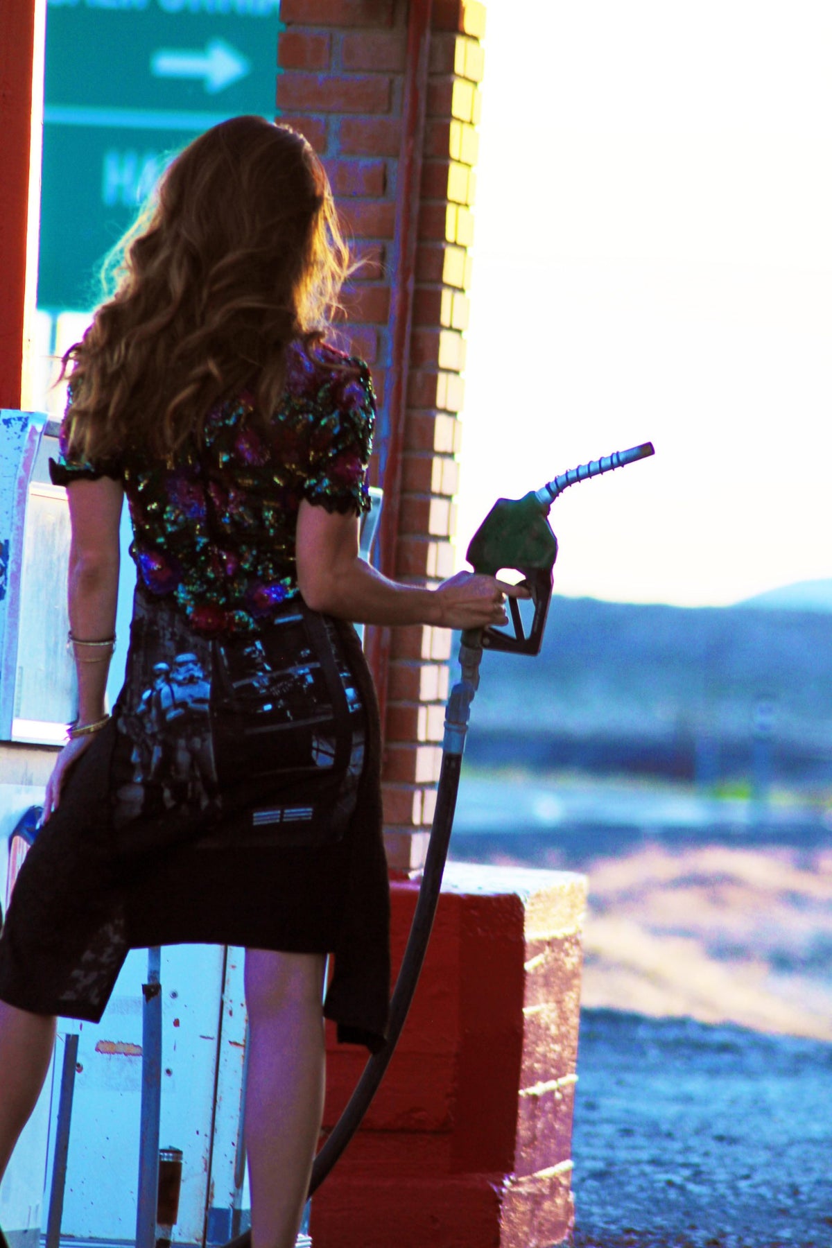 a woman pumping gas into her car at a gas station.