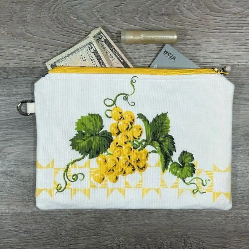 A white pouch with a floral pattern containing cash and a tube, placed on a wood-textured surface.