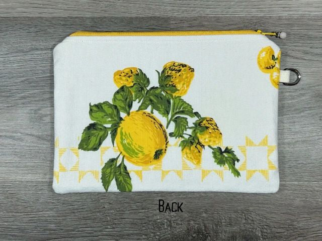 A white zippered pouch with a painted design of yellow flowers and green leaves, displayed on a gray wooden surface.