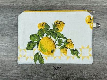 A white zippered pouch with a painted design of yellow flowers and green leaves, displayed on a gray wooden surface.