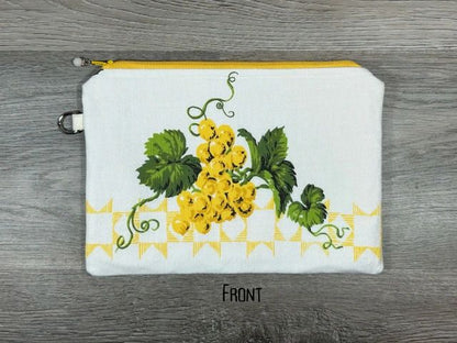 White fabric pouch with a floral pattern featuring yellow flowers and green leaves, displayed on a gray wooden surface.