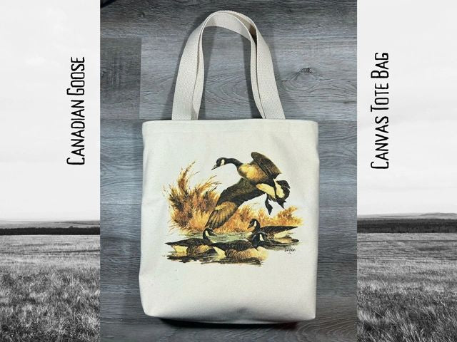 Canvas tote bag with a printed image of canadian geese on a grassy field, placed against a grayscale wooden background. text "canadian goose" and "canvas tote bag" at the top.