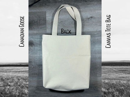 White canvas tote bag with "back" printed on it, displayed against a black and white rural landscape background. text reads "canadian goose canvas tote bag".