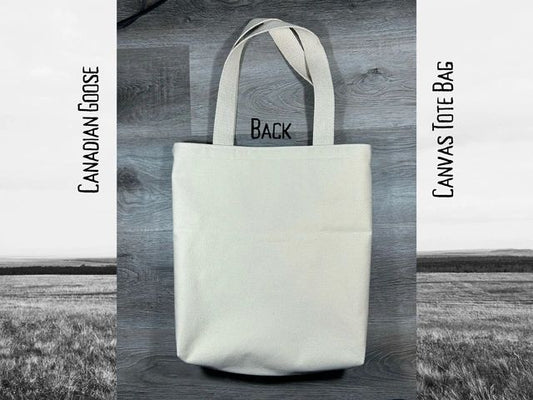 White canvas tote bag with "back" printed on it, displayed against a black and white rural landscape background. text reads "canadian goose canvas tote bag".