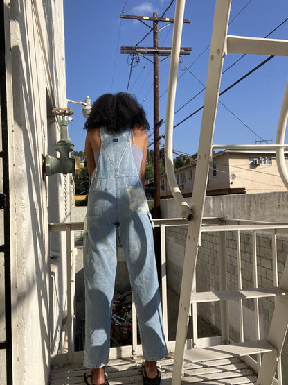 A woman standing on a ladder in overalls.