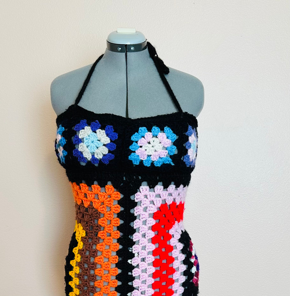 A colorful crocheted dress on a mannequin dummy.