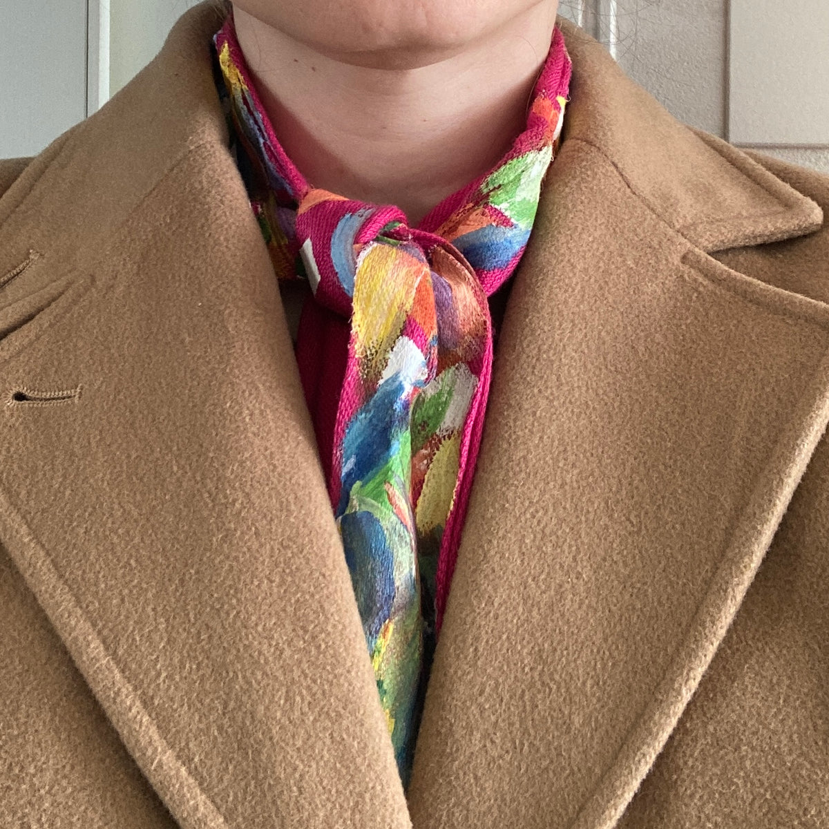 A woman in a tan coat with a hand-painted scarf.