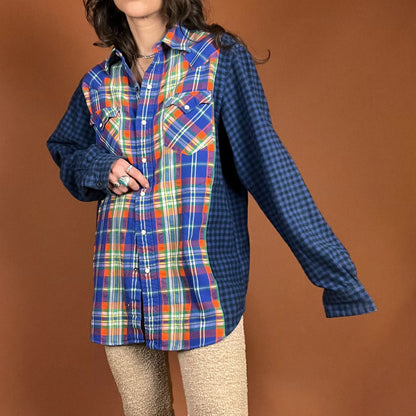 A woman in The Plaid Flannel Mash Up Button Down Shirt In Blue/Orange poses for a picture.