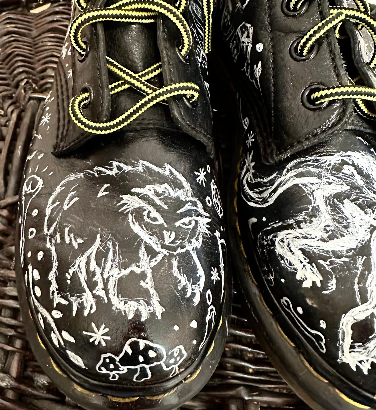 A pair of black dr martens shoes with doodles on them.