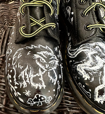 A pair of black dr martens shoes with doodles on them.