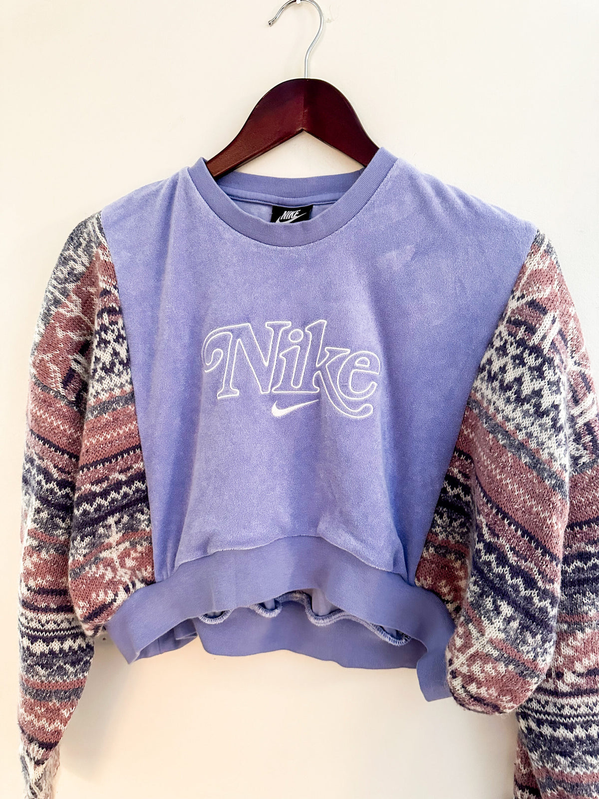 A purple nike cropped sweater hanging on a hanger.