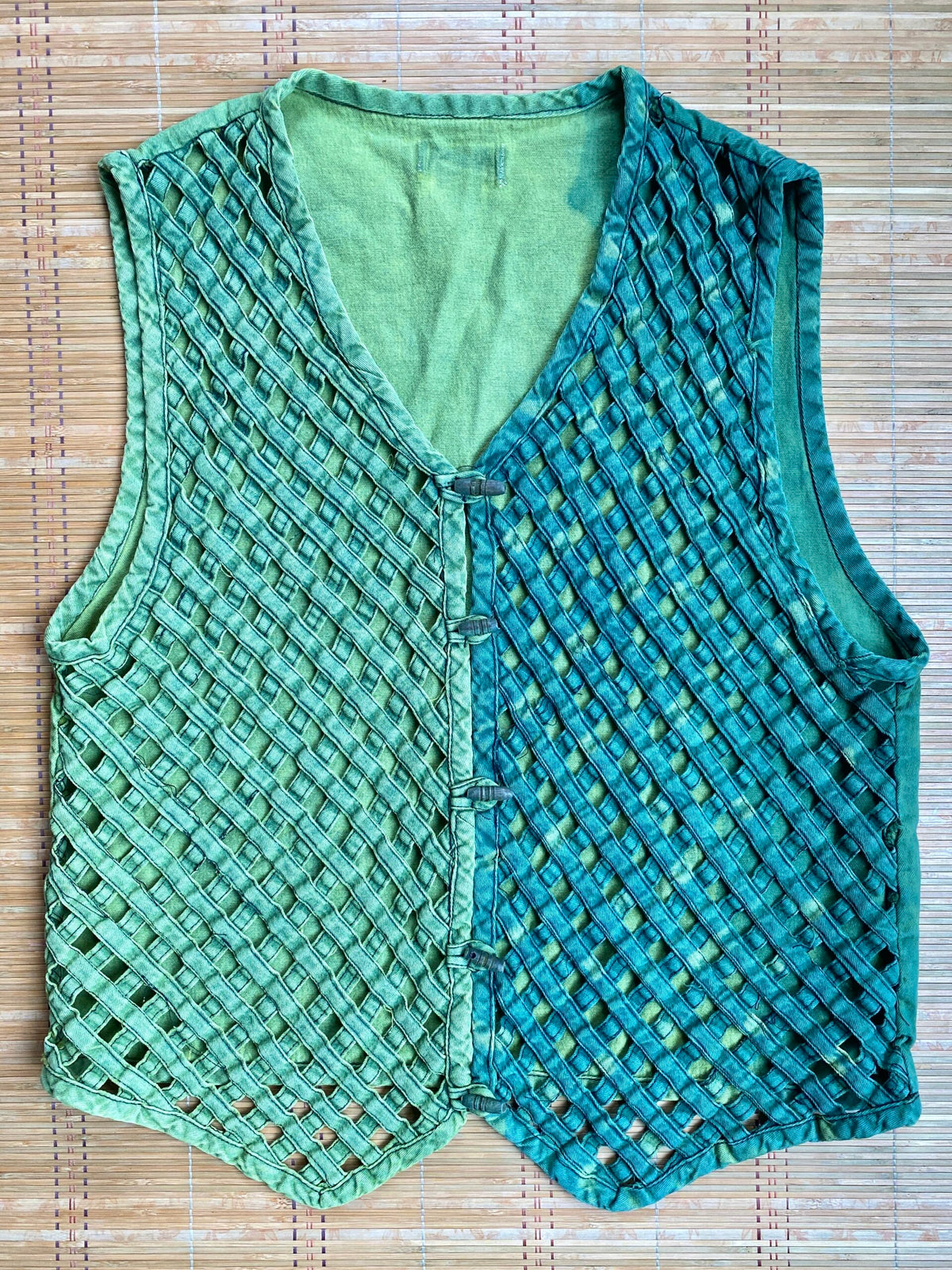 A green knitted vest on a bamboo mat.