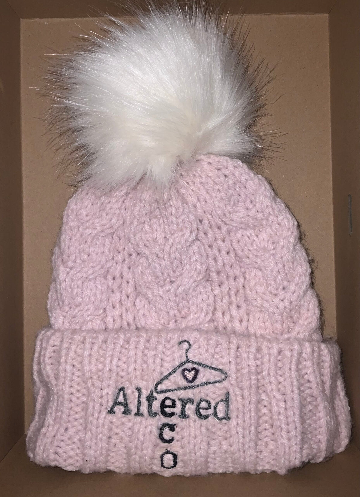 A pink knitted beanie with a white pom pom.