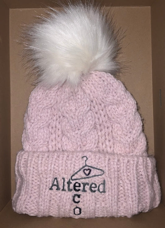 A pink knitted beanie with a white pom pom.