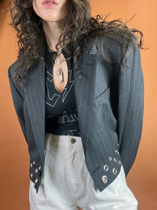 Woman wearing a pinstripe blazer with a graphic tee and light-colored pants, accessorized with a necklace.