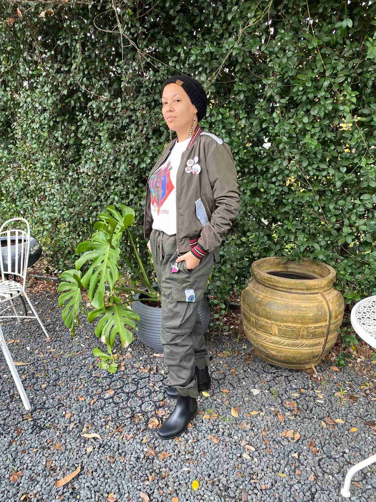 a woman standing in front of a bush holding a potted plant.